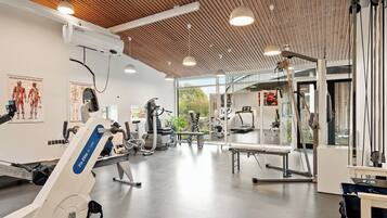 Une salle de sport équipée de divers appareils d’exercice, dotée d’un plafond en bois et de grandes fenêtres.