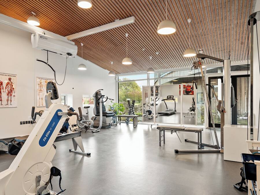 Une salle de sport équipée de divers appareils d’exercice, dotée d’un plafond en bois et de grandes fenêtres.