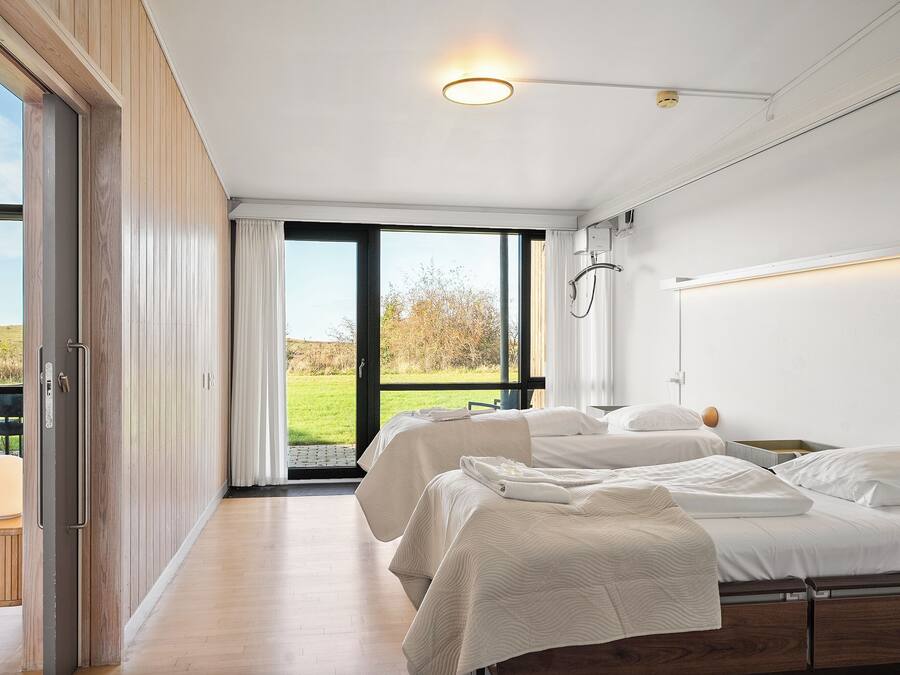 Une chambre d’hôtel moderne dotée d’une grande porte-fenêtre coulissante donnant sur un espace extérieur, d’un lit avec une literie blanche et d’une table de chevet.
