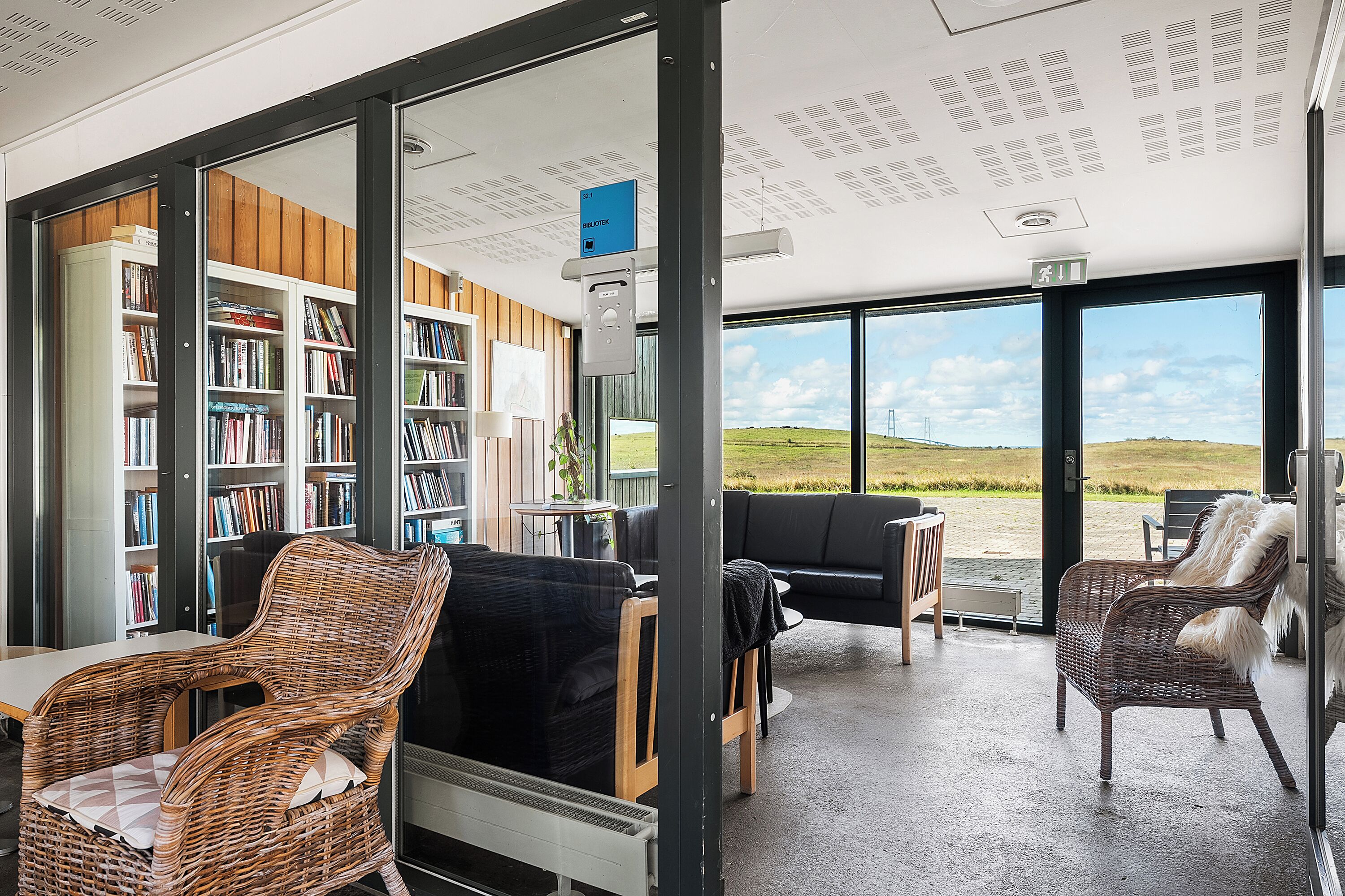Una habitación con una amplia estantería, muebles de mimbre y vistas a un campo verde a través de grandes ventanales.