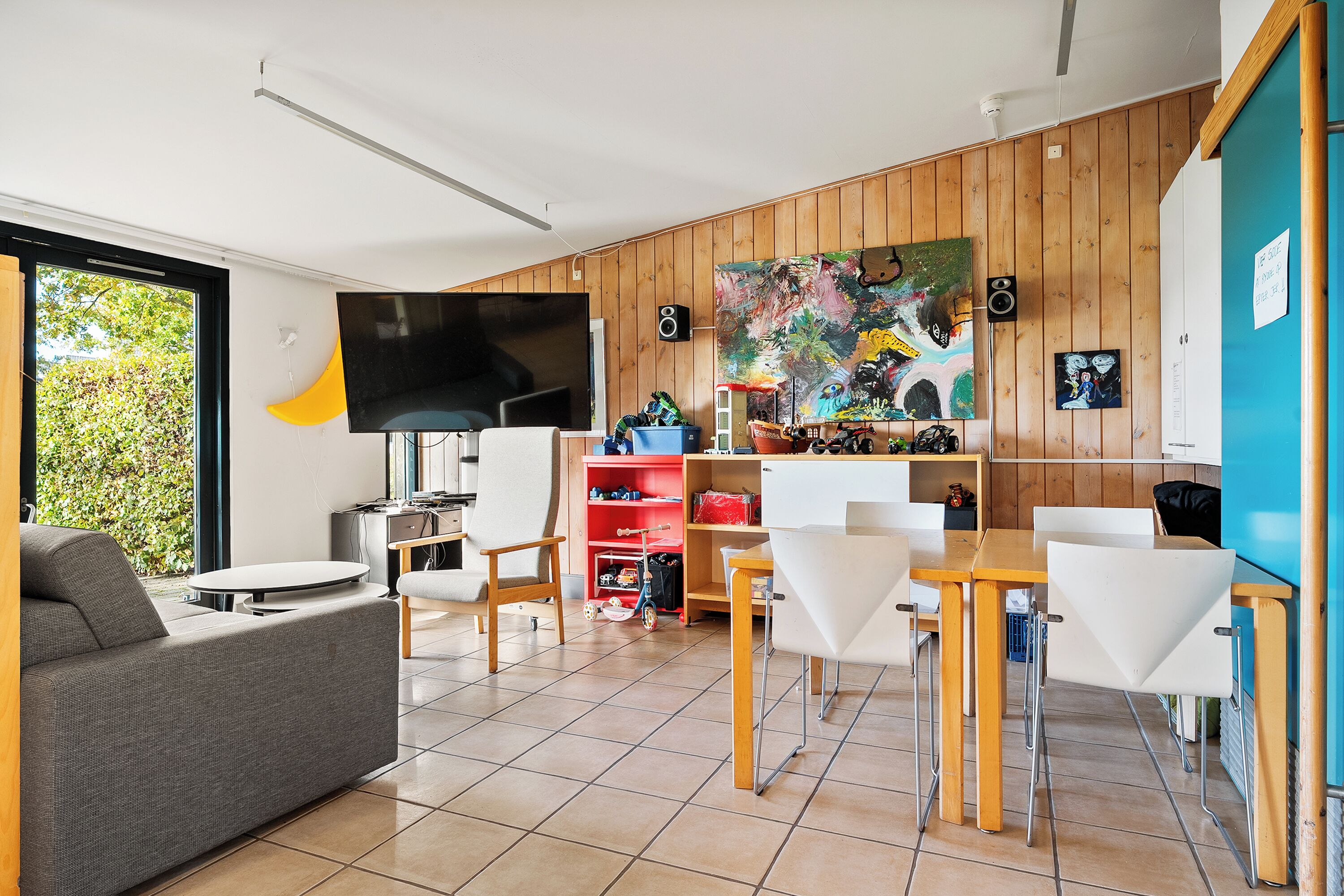 Un salon moderne comprenant un canapé, une table à manger, des chaises, un téléviseur et un coin cuisine avec des meubles en bois et un tableau.