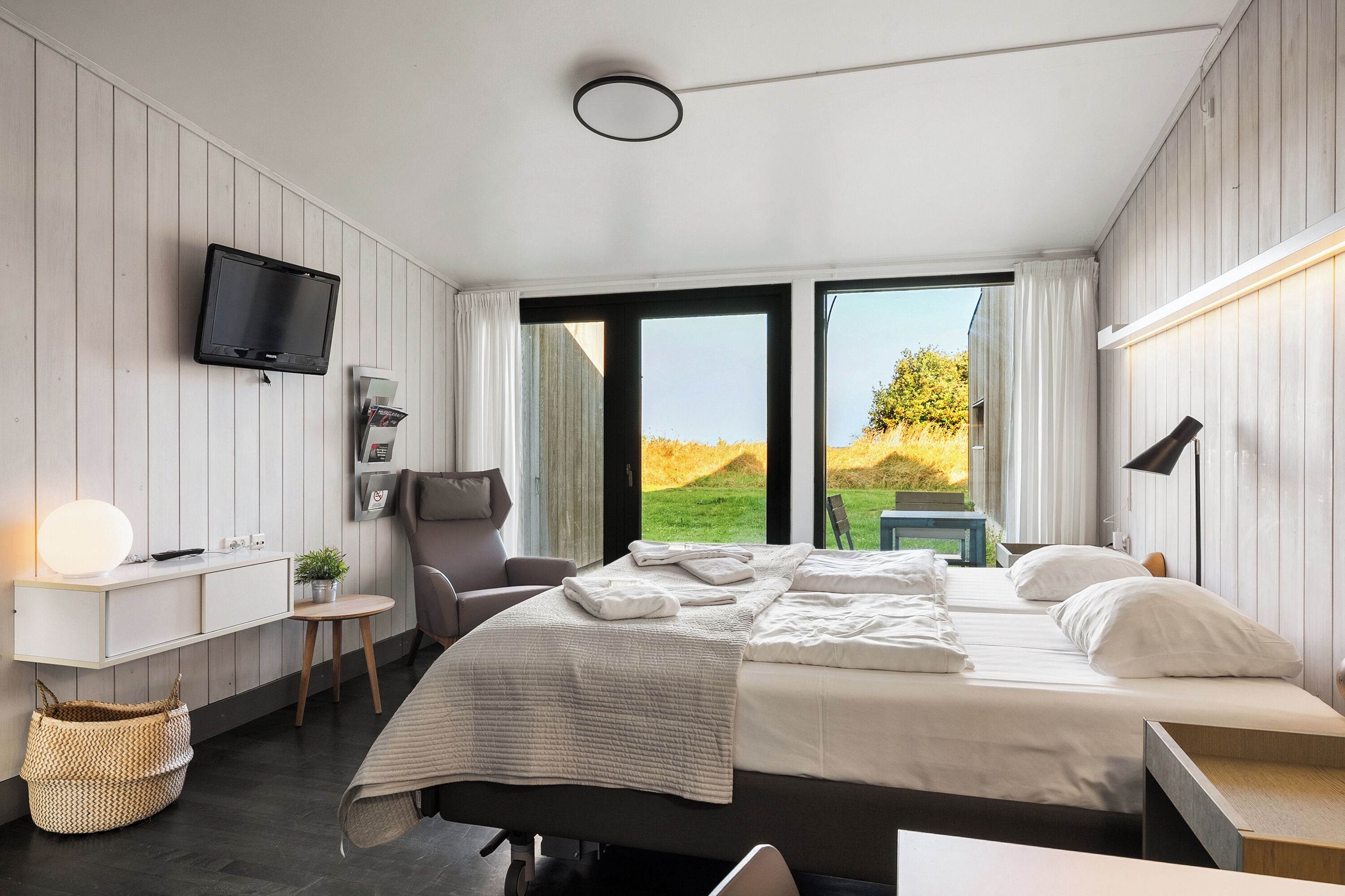 A modern bedroom with a bed, bedside table, TV, and a view of the outdoors.