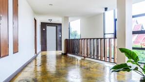 A hallway with a polished concrete floor, wooden doors, and a balcony with a metal railing. - Sunshine House (Chiang Mai)