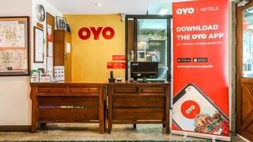 Una reception con un grande cartello OYO Hotels, un computer e un banner promozionale rosso per l'app OYO.