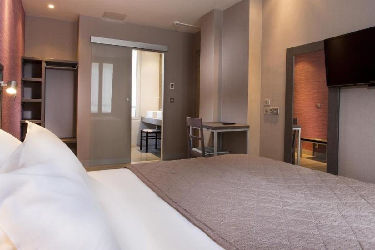 Une chambre d’hôtel avec un lit, un bureau, une chaise, une télévision et une salle de bain visible à travers une porte ouverte.