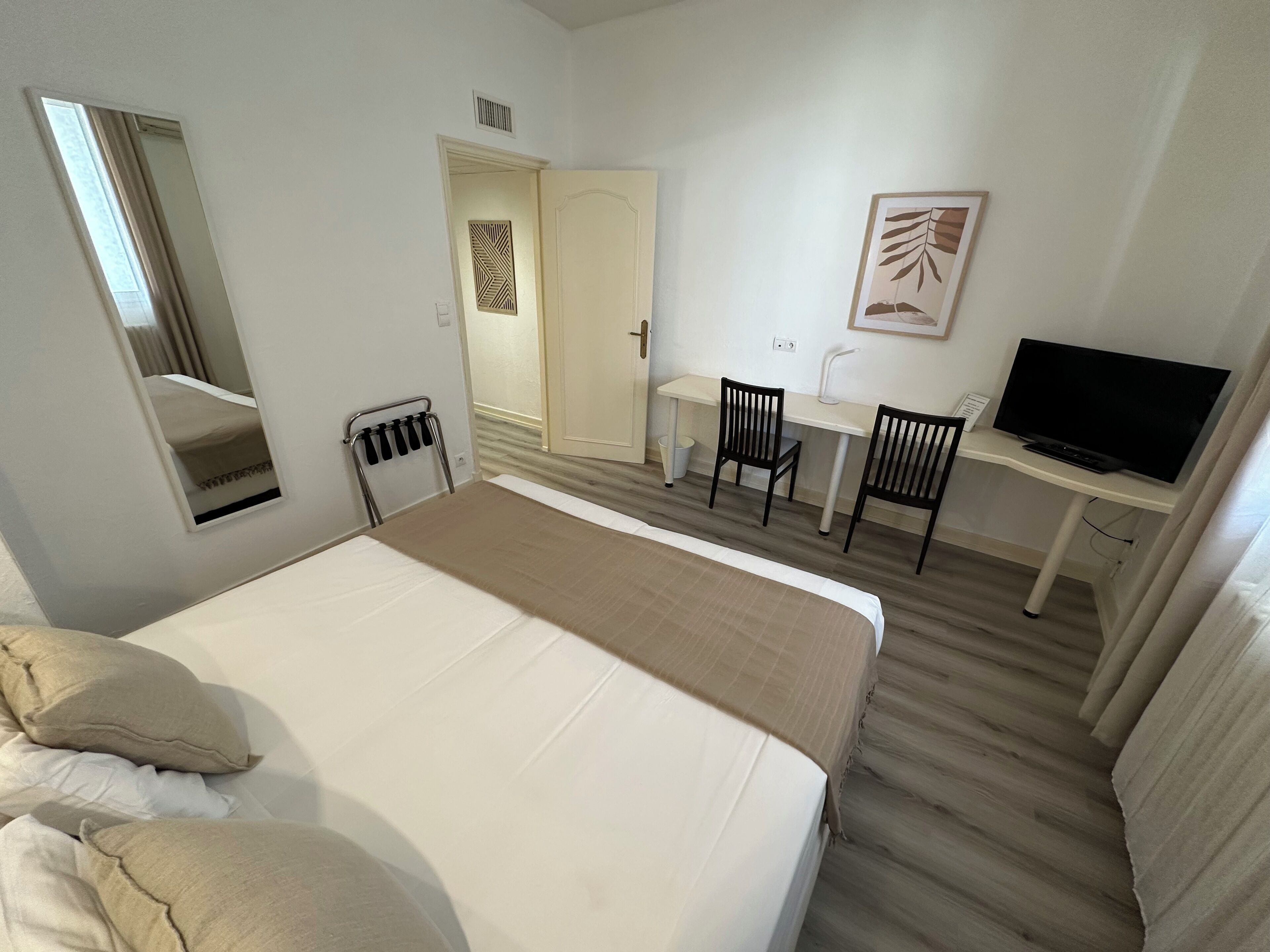 A hotel room with a large bed, a desk with two chairs, a television, and a mirror.