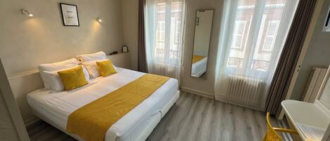 A hotel room with a bed, a chair, a desk, a mirror, and a window with curtains.