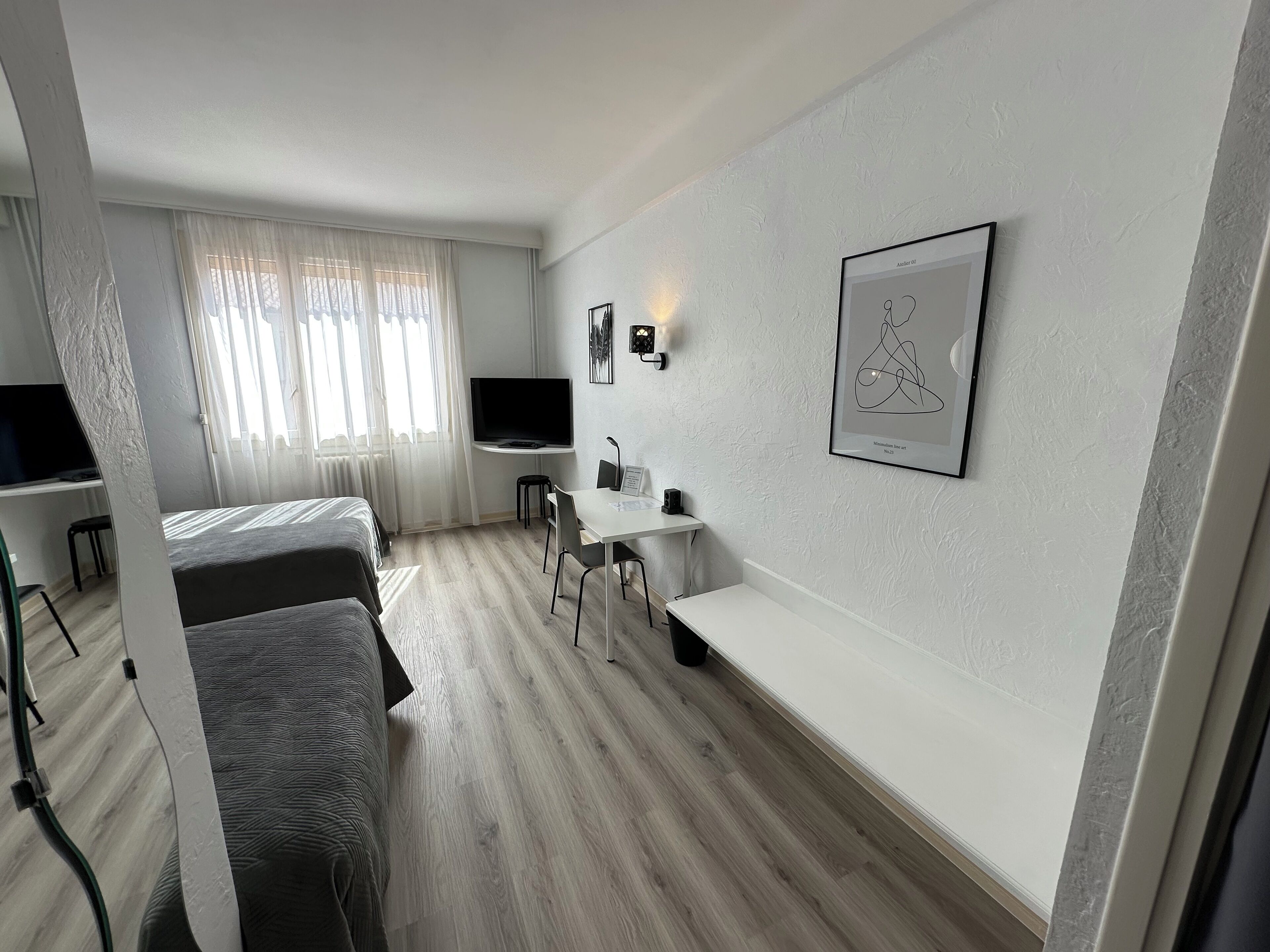 Et moderne hotelværelse med seng, skrivebord, stol, fjernsyn og et billede i ramme på væggen.