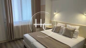 Een hotelkamer met een bed, gordijnen, een nachtkastje en een aan de muur bevestigd lampje.