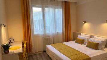 A hotel room with a bed, bedside tables, a chair, a potted plant, and a window with curtains.