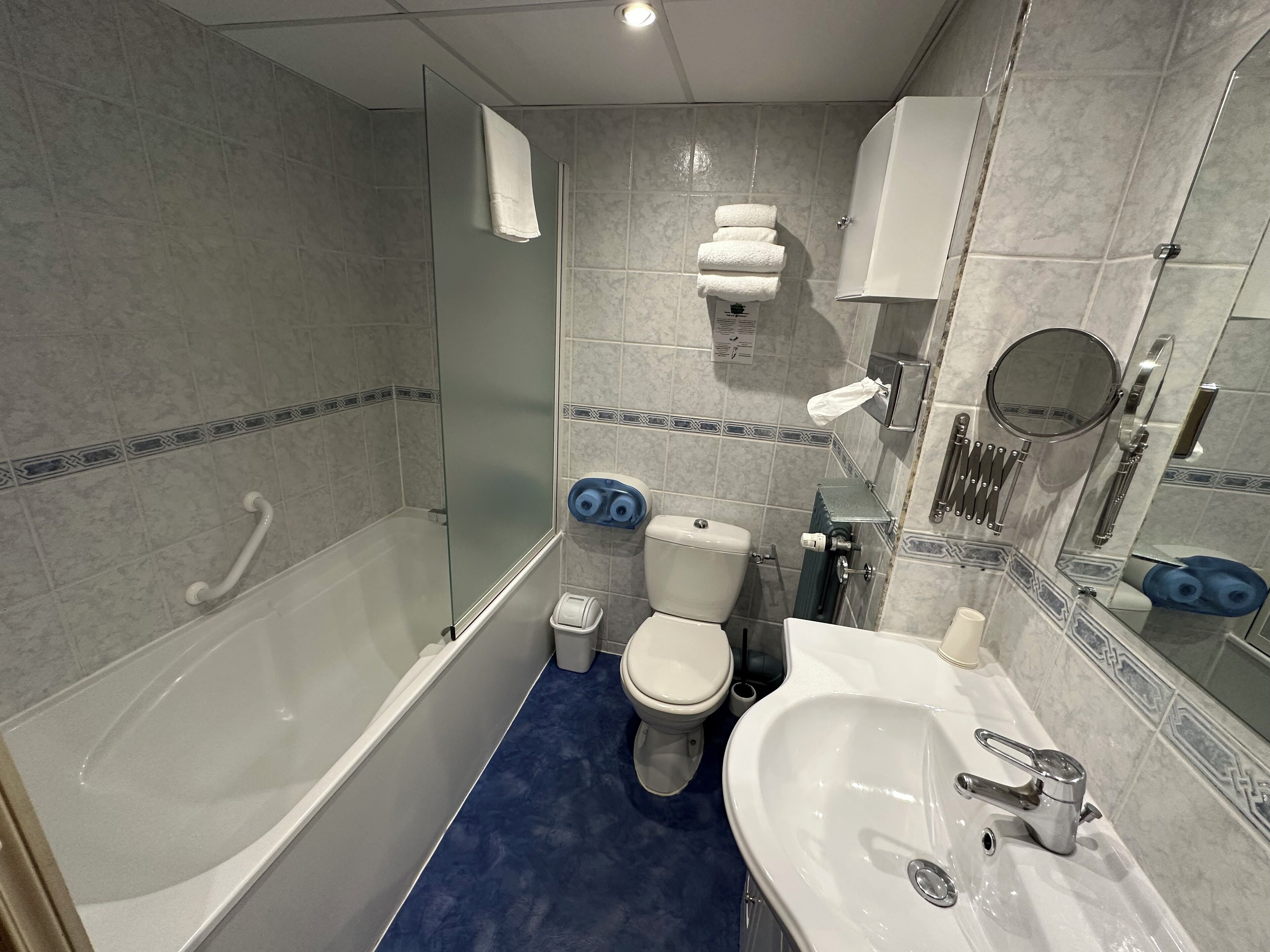 A bathroom with a bathtub, toilet, and sink, featuring a blue floor and tiled walls.