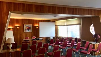 A conference room with red chairs, a whiteboard, and a projector screen.
