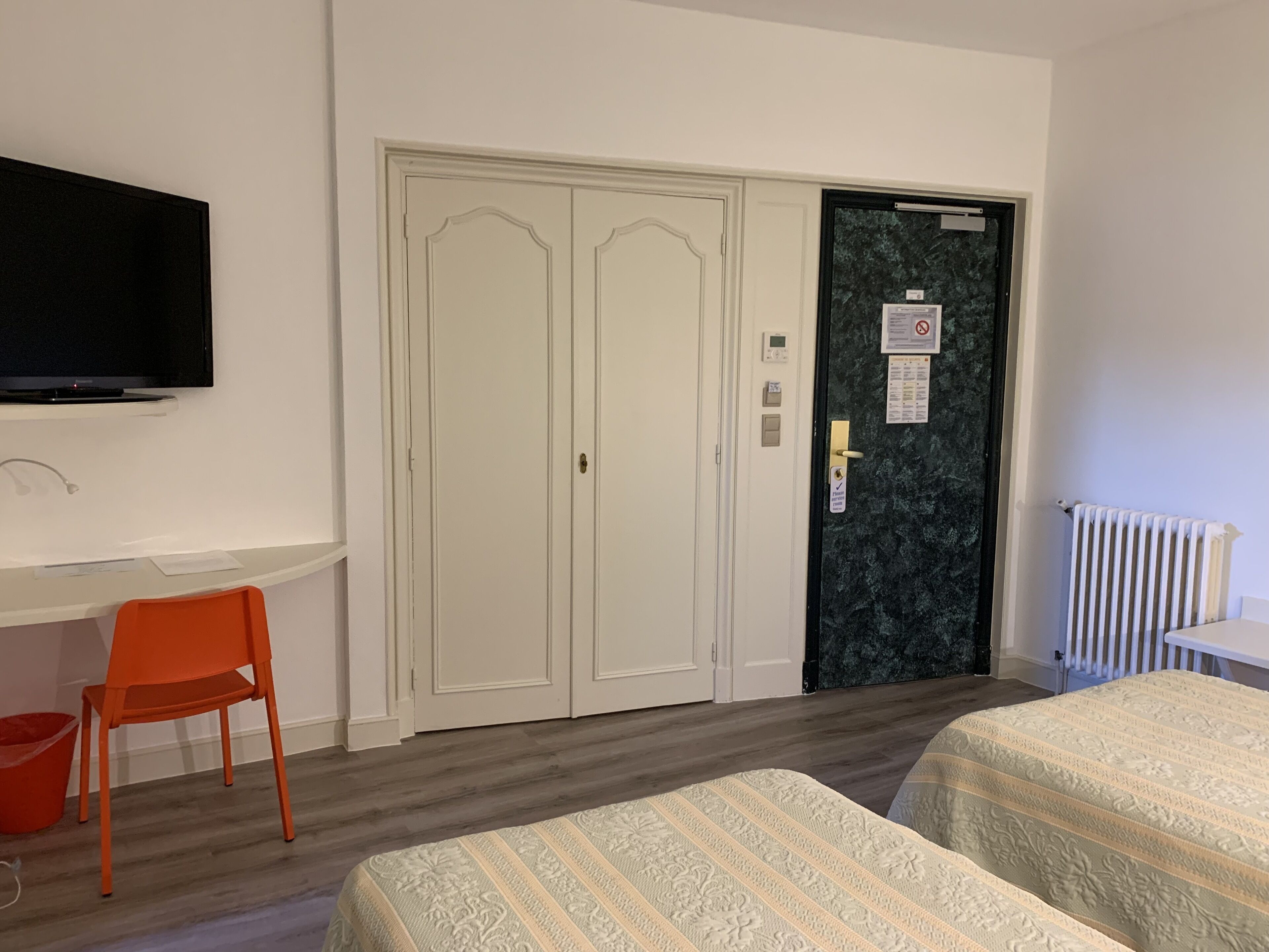 A hotel room with a bed, a desk with a chair, a television, a wardrobe, and a door with a security card reader.