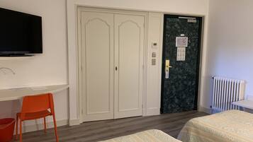 A hotel room with a bed, a desk with a chair, a television, a wardrobe, and a door with a security card reader.