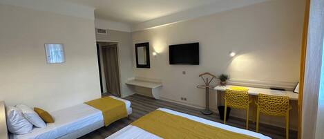 A hotel room with two beds, a desk, a chair, a TV, and a small plant.
