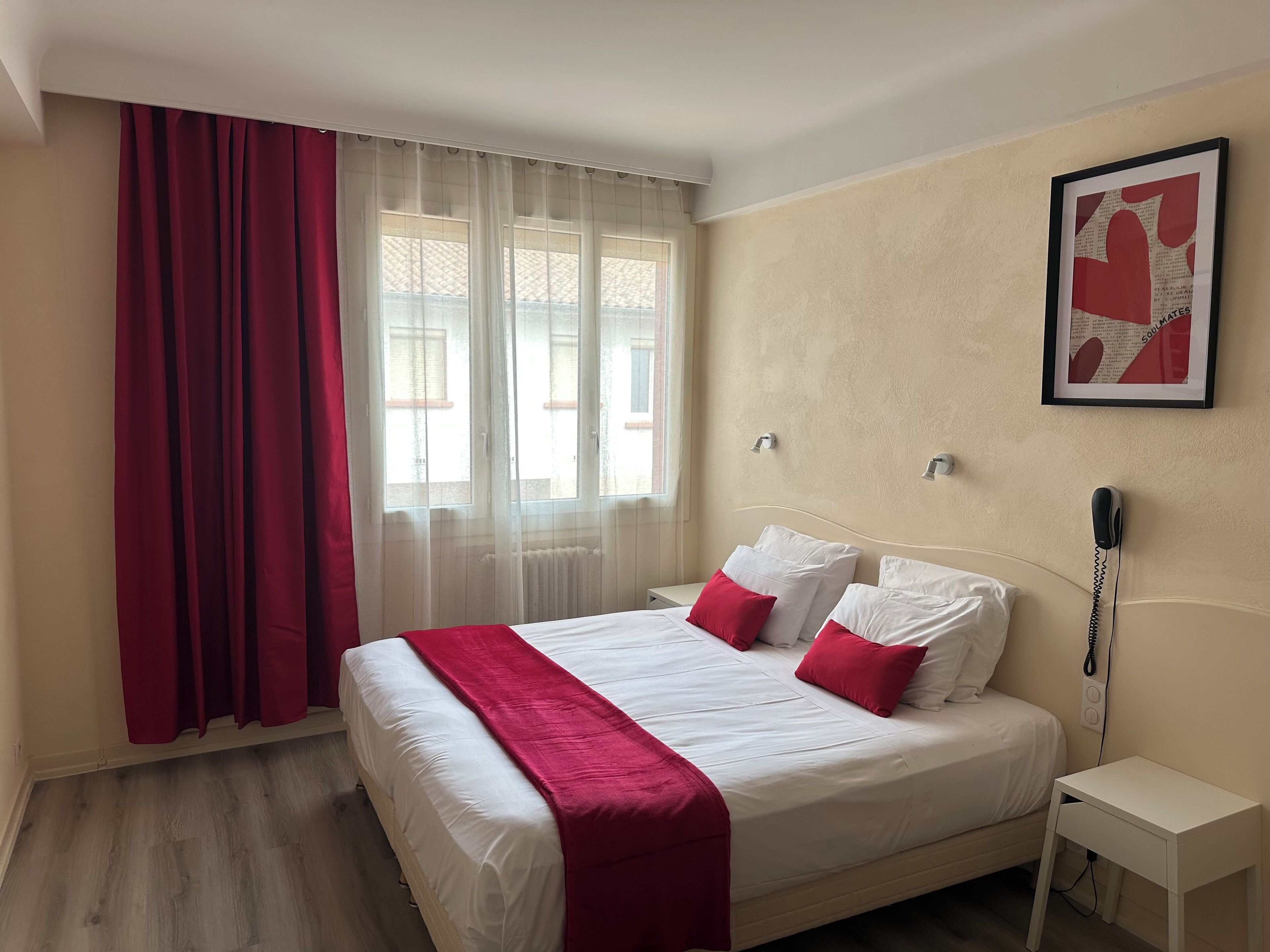 A hotel room with a bed, a bedside table, a phone, and a window with curtains.