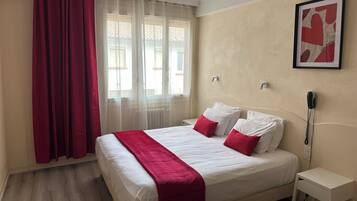 A hotel room with a bed, a bedside table, a phone, and a window with curtains.