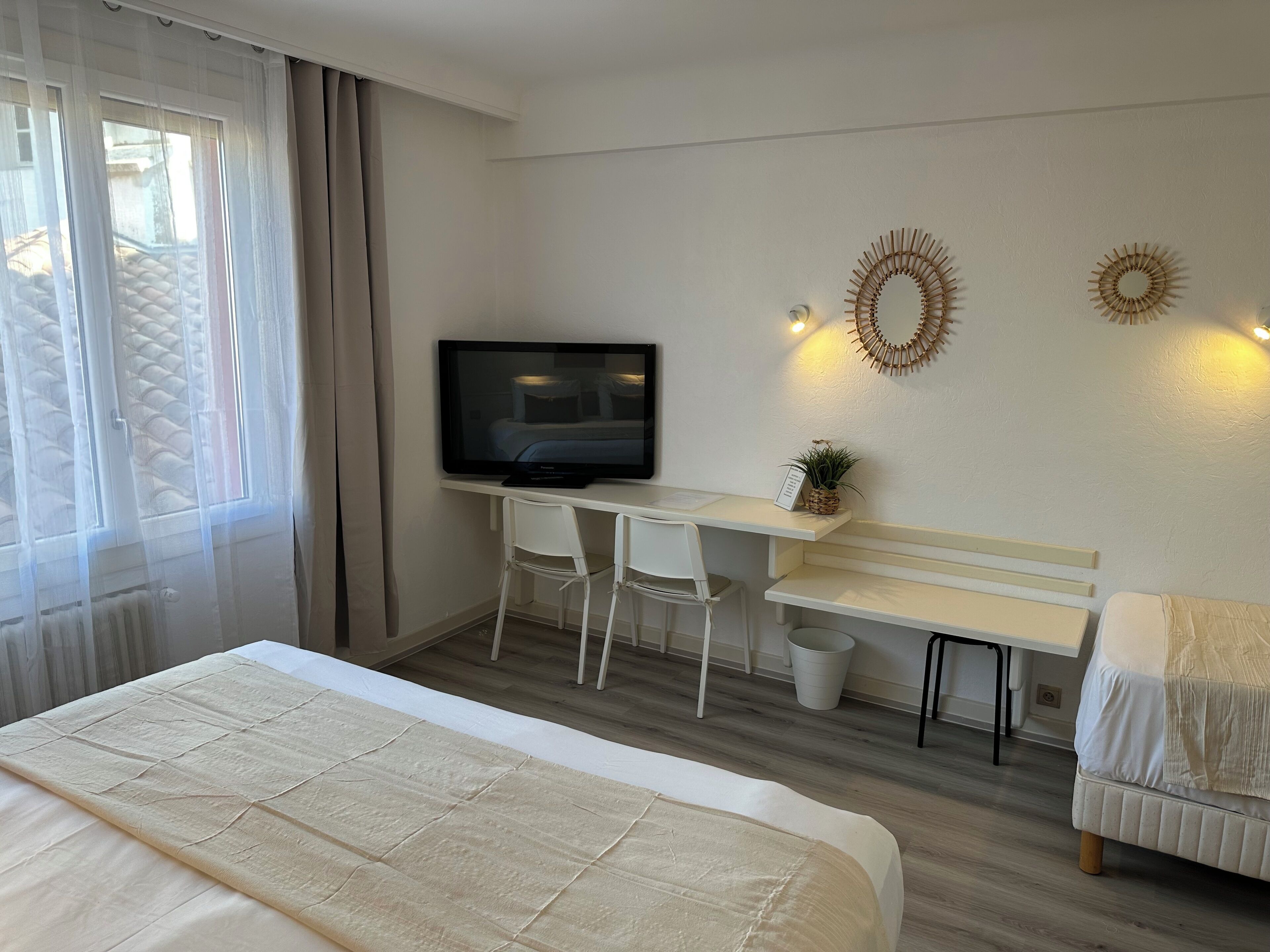 Een hotelkamer met een bed, een bureau met een televisie, twee stoelen, een klein tafeltje en decoratieve wandkunst.