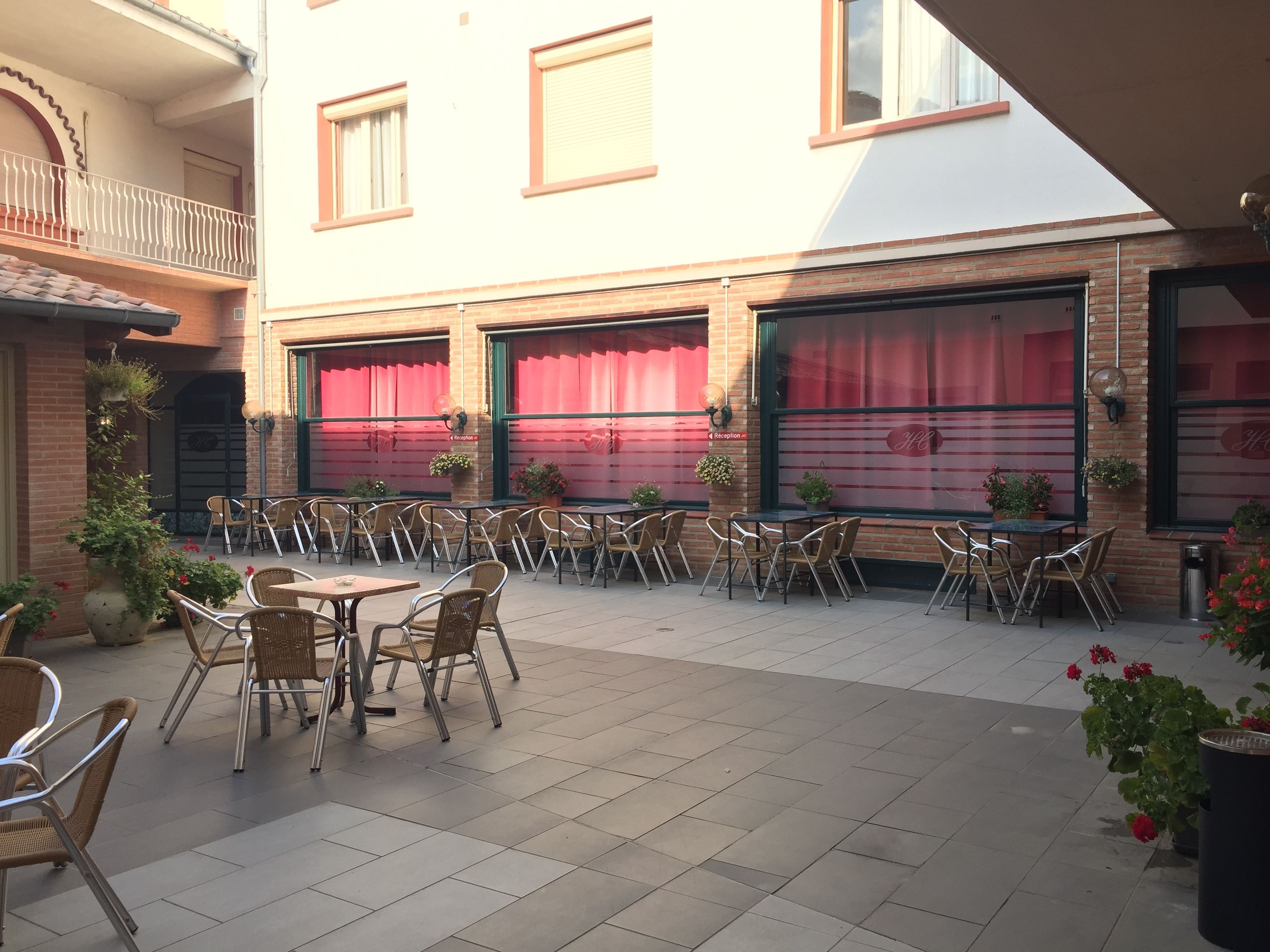 An outdoor patio with multiple tables and chairs, a brick wall, and potted plants.