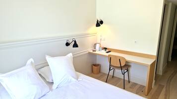 Ett hotellrum med en säng, ett skrivbord, en stol, en lampa och en papperskorg.