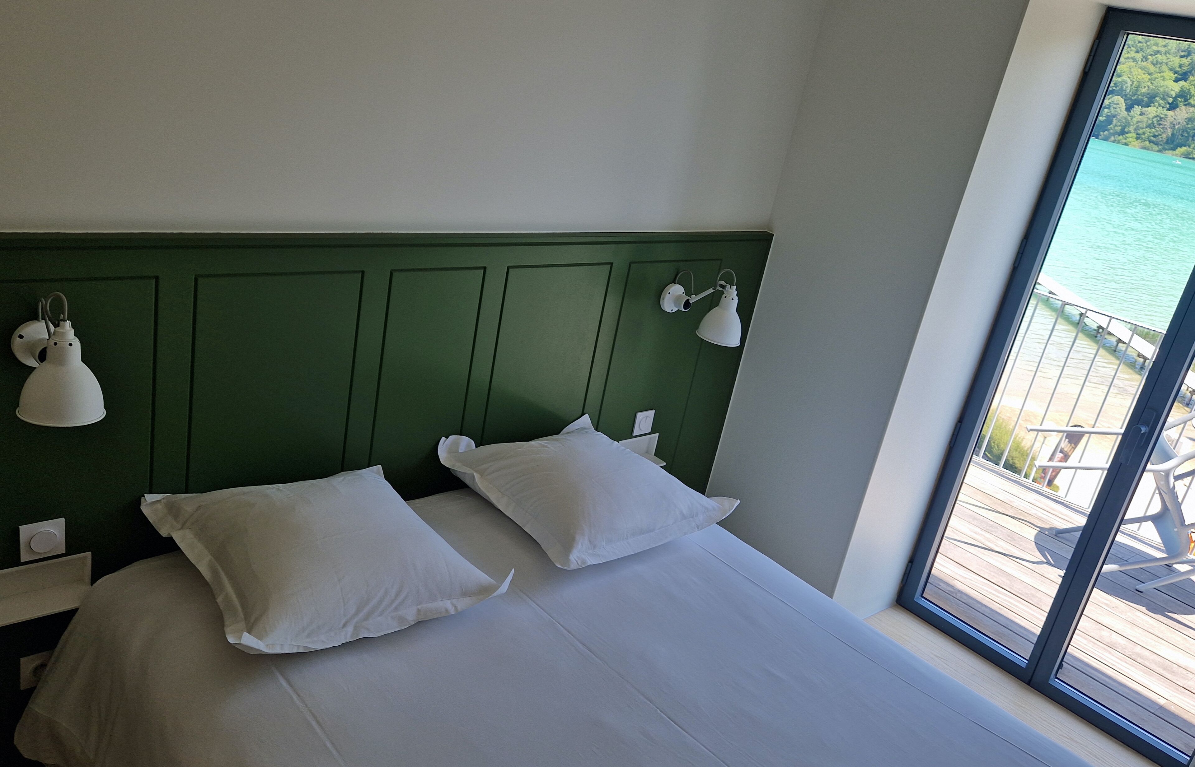 A bed with white bedding and pillows, a green headboard, and two wall-mounted lamps.
