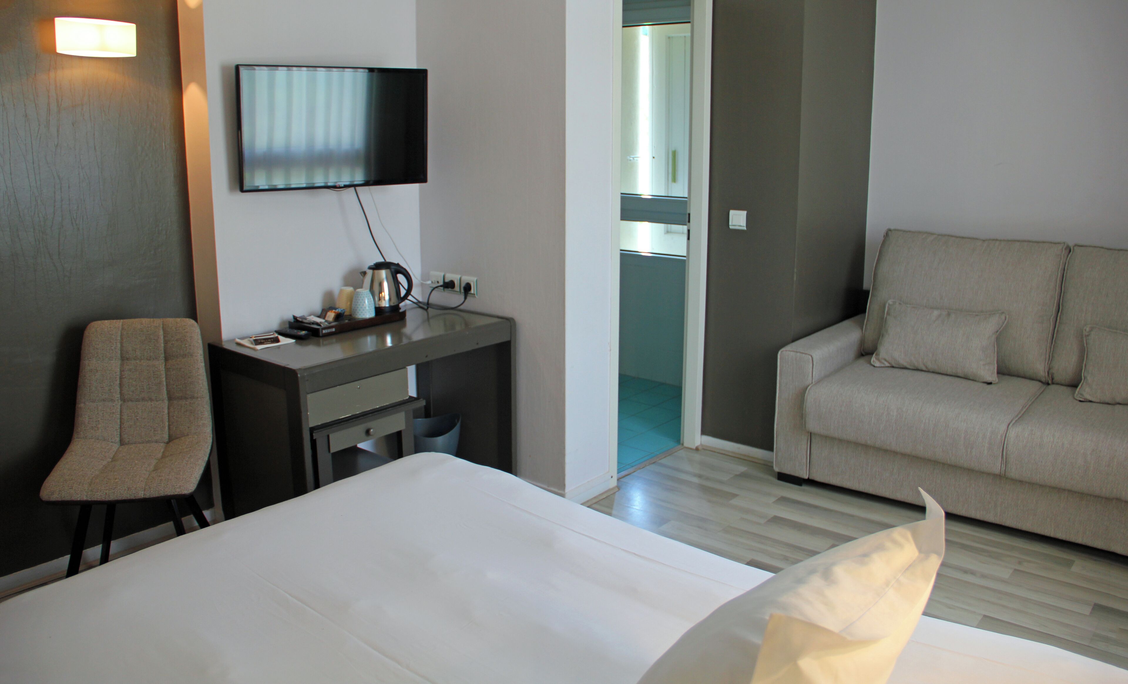 A hotel room with a bed, a desk with a television, a chair, and a sofa.