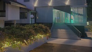 Un edificio moderno con fachada geométrica, una escalera que conduce a un nivel superior y un área de entrada bien iluminada.