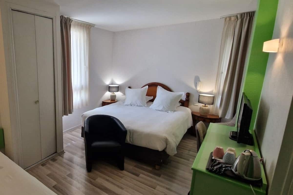 A hotel room with a bed, bedside tables, a desk with a chair, a wardrobe, and a television.