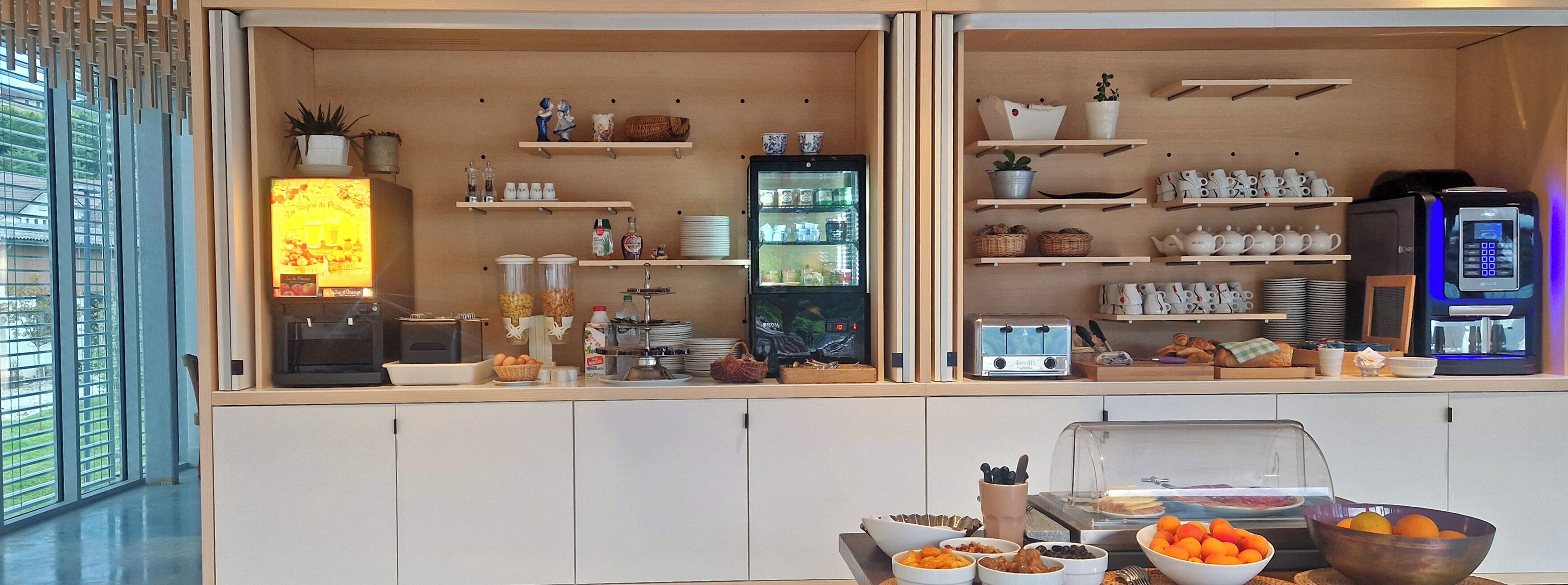 Una barra de desayuno con diferentes opciones de alimentos, un refrigerador y una cafetera.