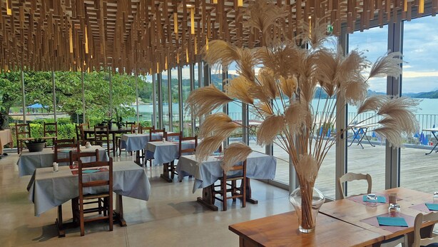 Un restaurante con mesas y sillas, techo de madera y vista a un lago.