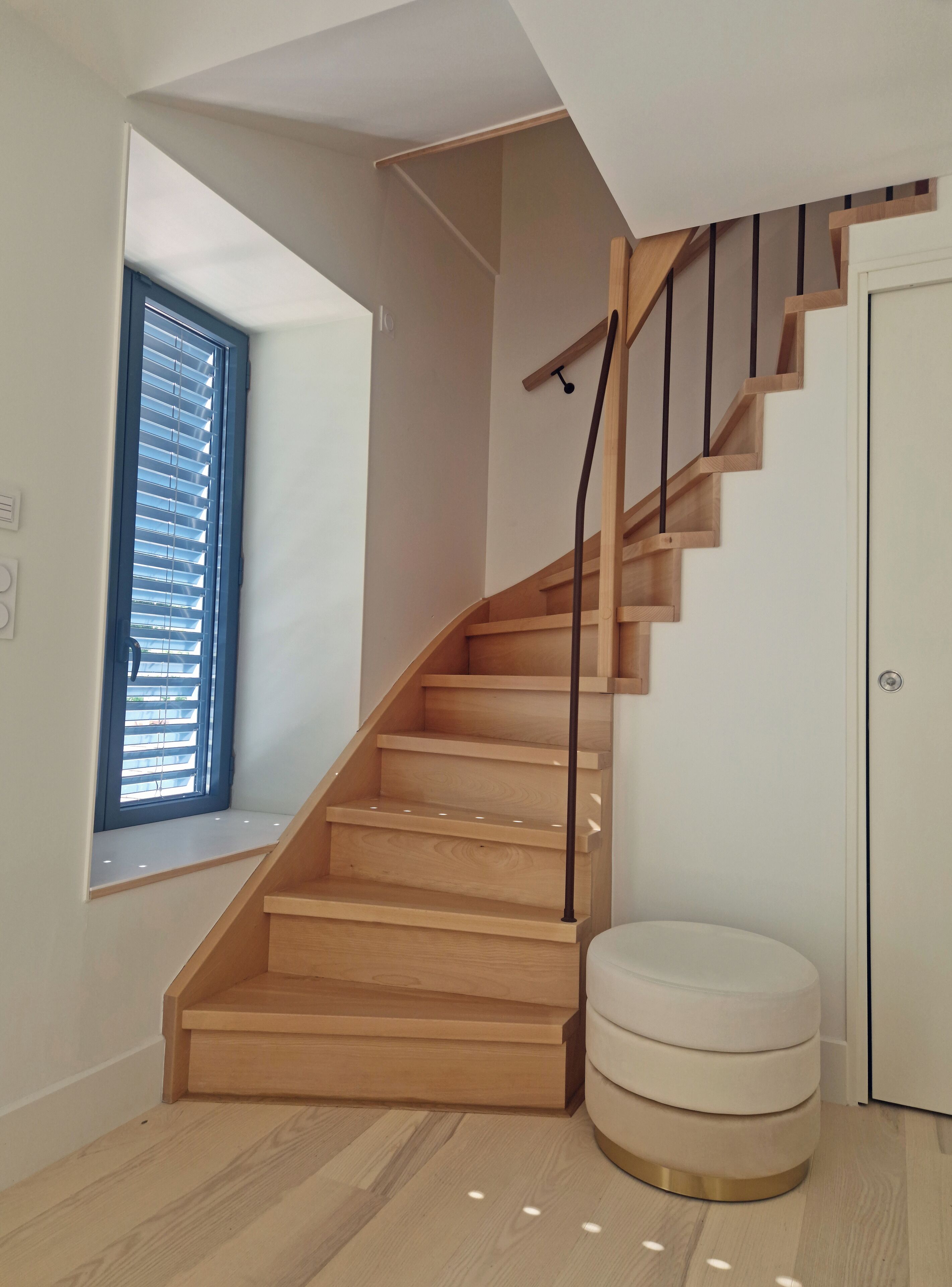 A wooden staircase with a black handrail, a white door, and a window with blinds.