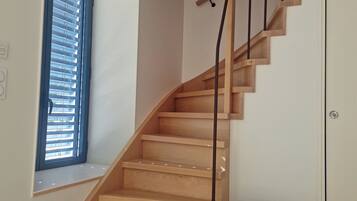 A wooden staircase with a black handrail, a white door, and a window with blinds.