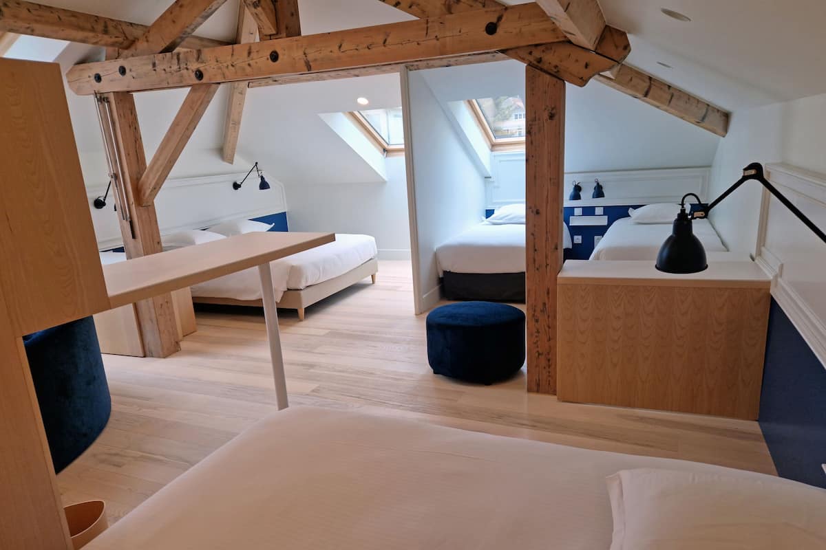 A loft-style bedroom with exposed wooden beams, a skylight, a bed, a desk, and a small bathroom.