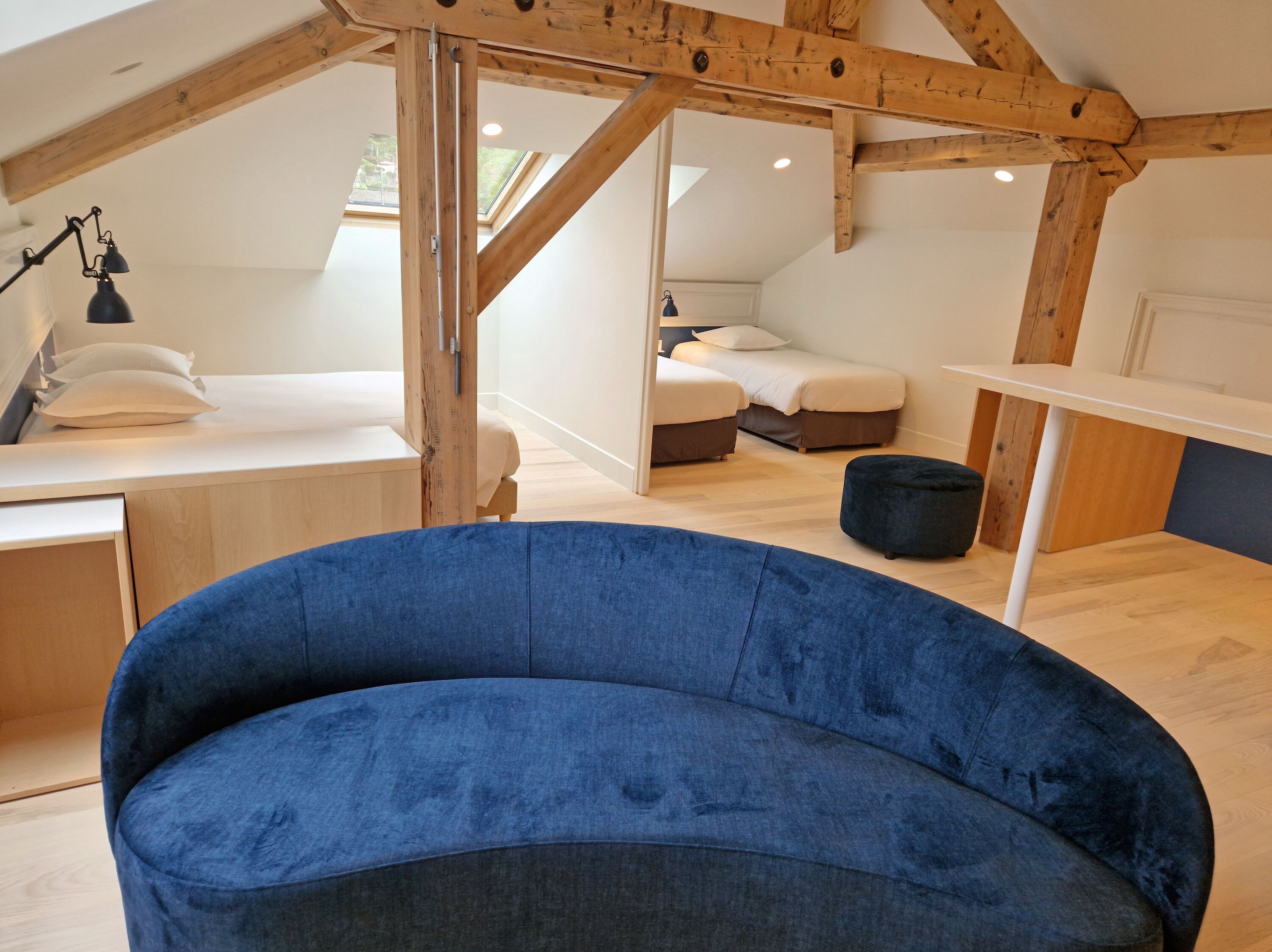 Un dormitorio tipo loft con techo inclinado, vigas de madera, un sofá azul, un escritorio y una cama con dos almohadas.