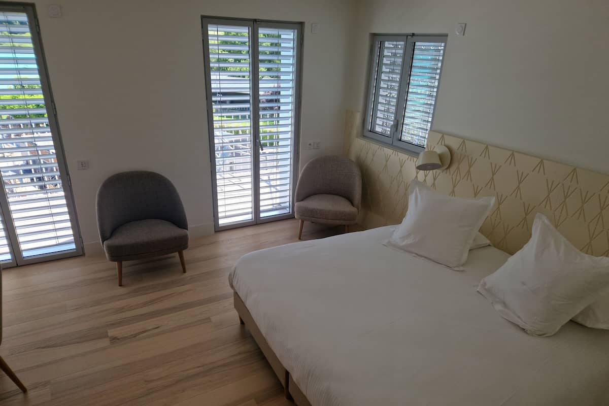 A bedroom with a bed, two chairs, a window, and a wall-mounted lamp.