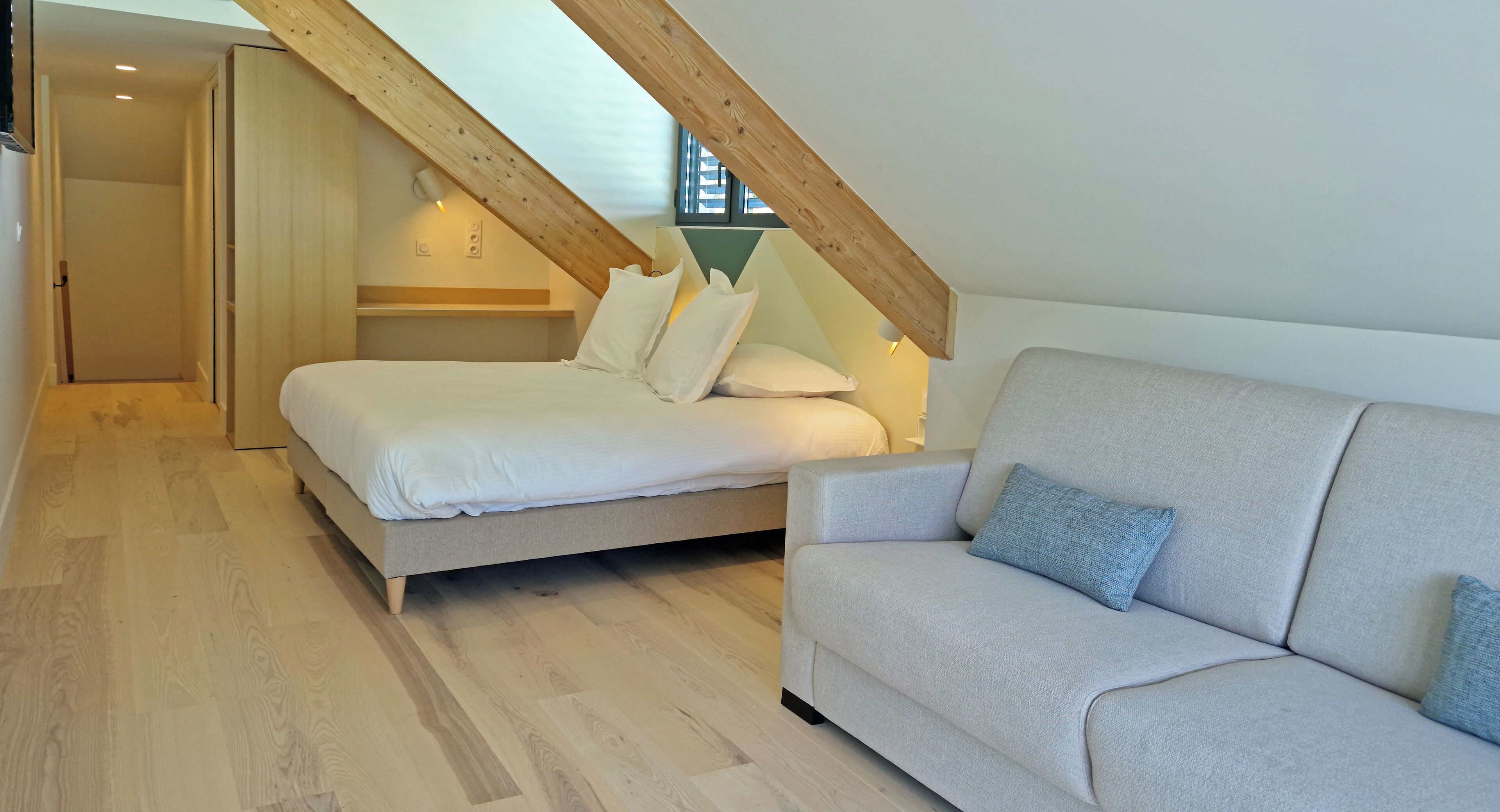 Un dormitorio con cama, sofá, vigas de madera y una ventana.