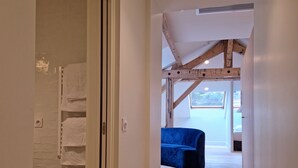 Un pasillo con una escalera de madera que lleva a una habitación con un sofá azul y un ventanal.