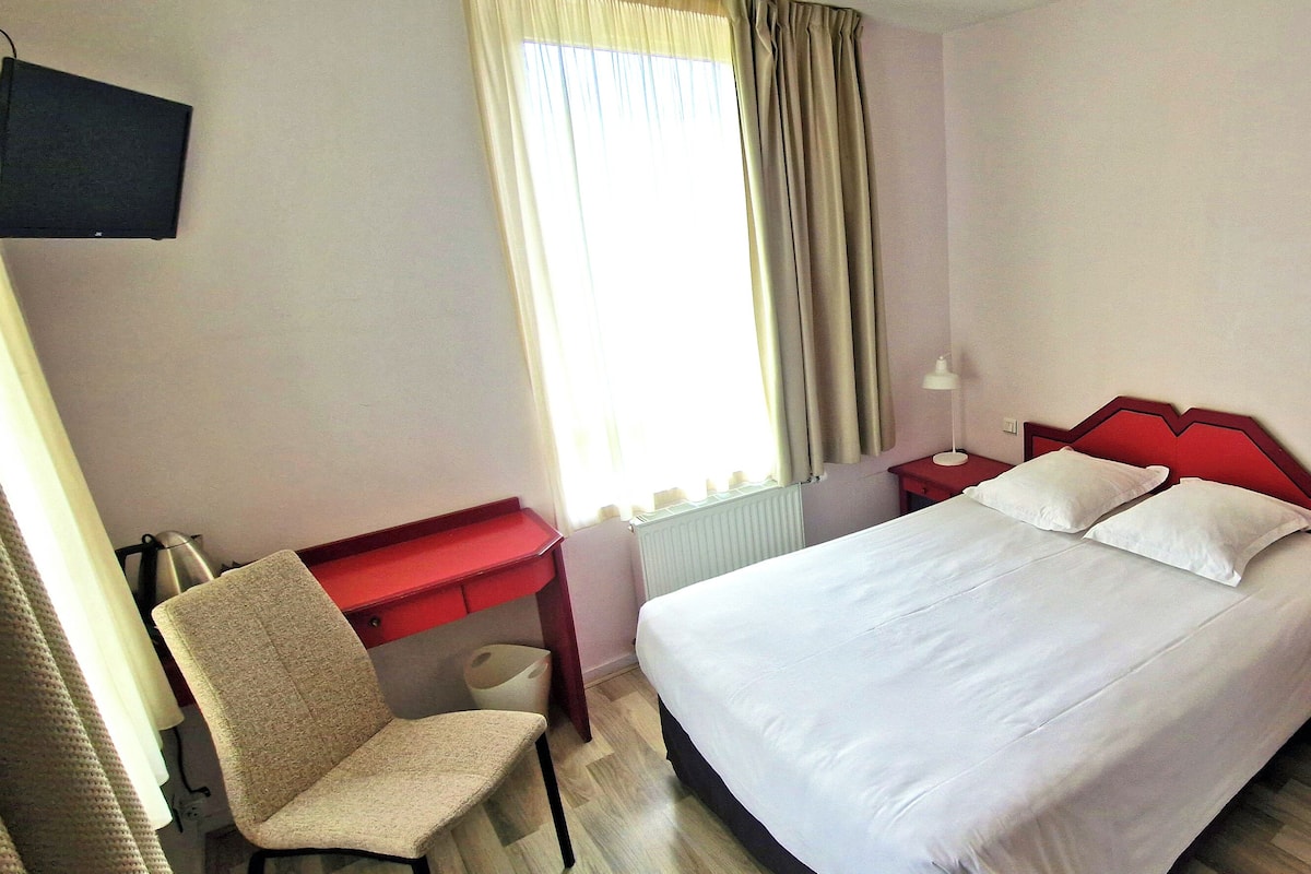 A hotel room with a bed, a chair, a desk, and a window with curtains.