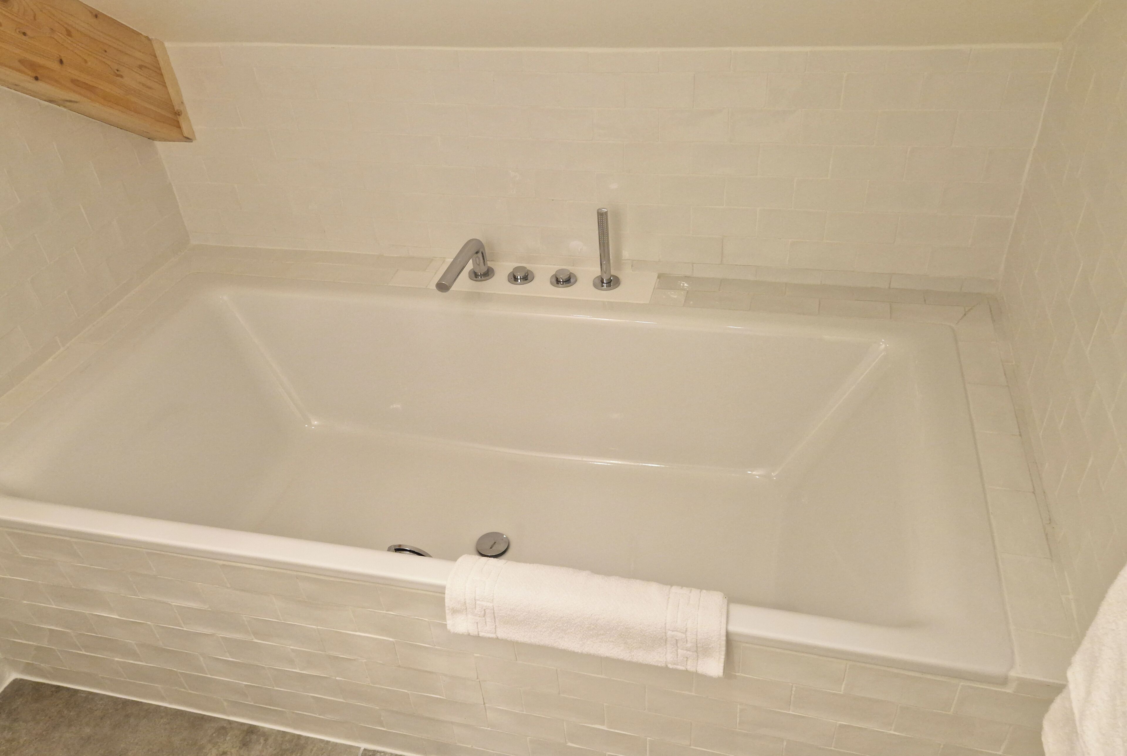 Eine rechteckige Badewanne mit einem weißen Handtuch an der Seite, vor einer weißen Ziegelwand.
