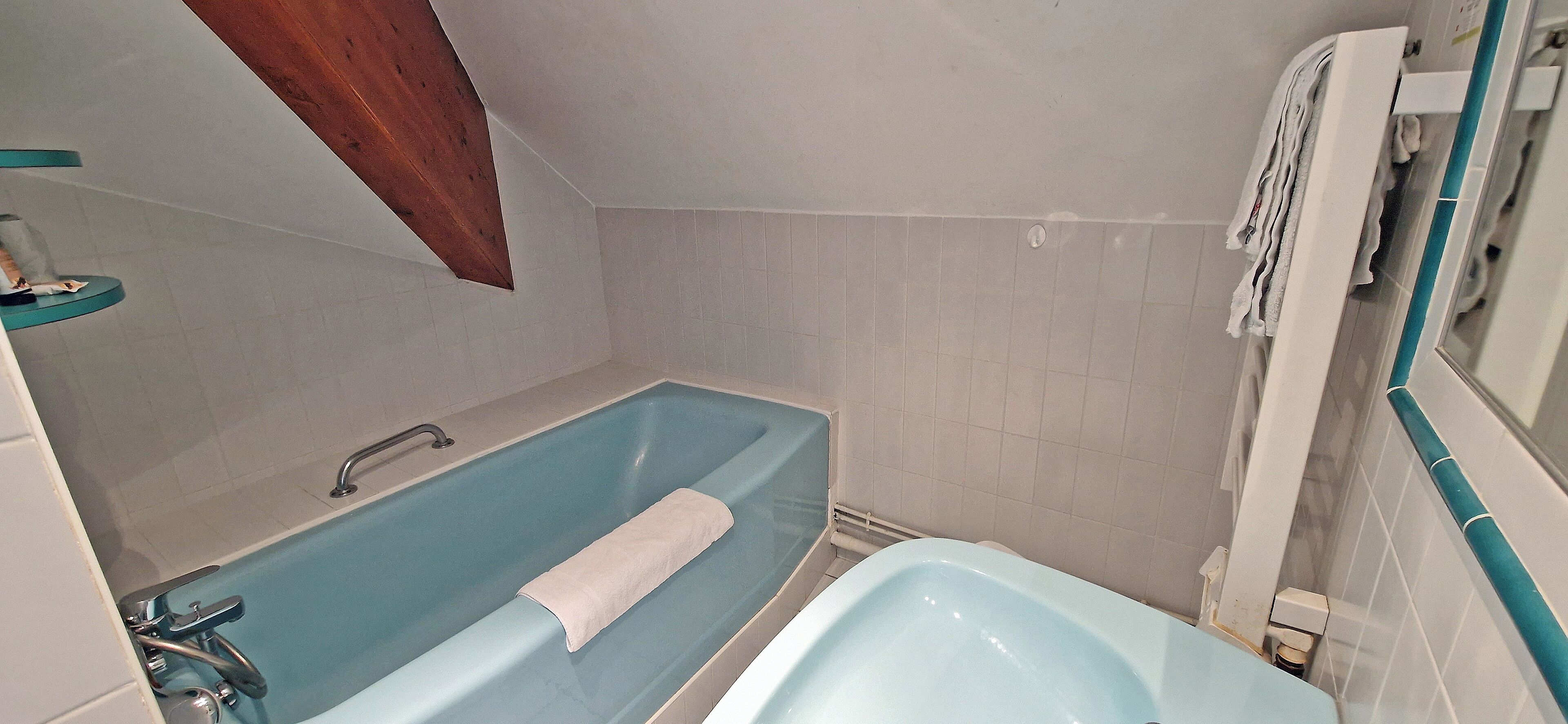 A bathroom with a blue bathtub, a white sink, and a wooden ceiling beam.