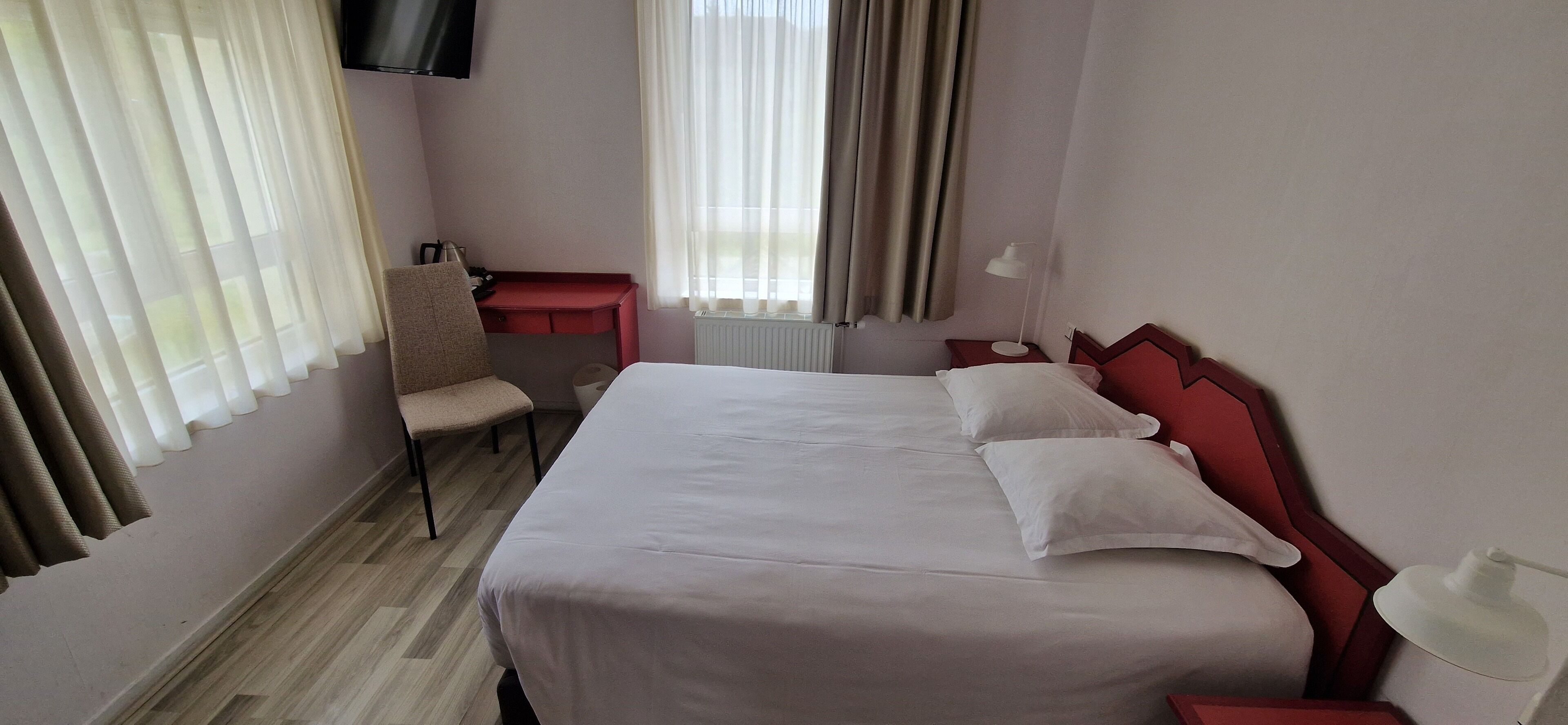 A hotel room with a large bed, a desk, a chair, and a TV mounted on the wall.