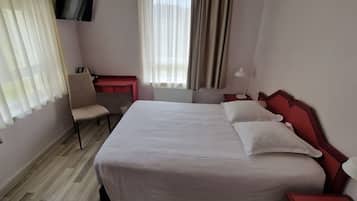 A hotel room with a large bed, a desk, a chair, and a TV mounted on the wall.