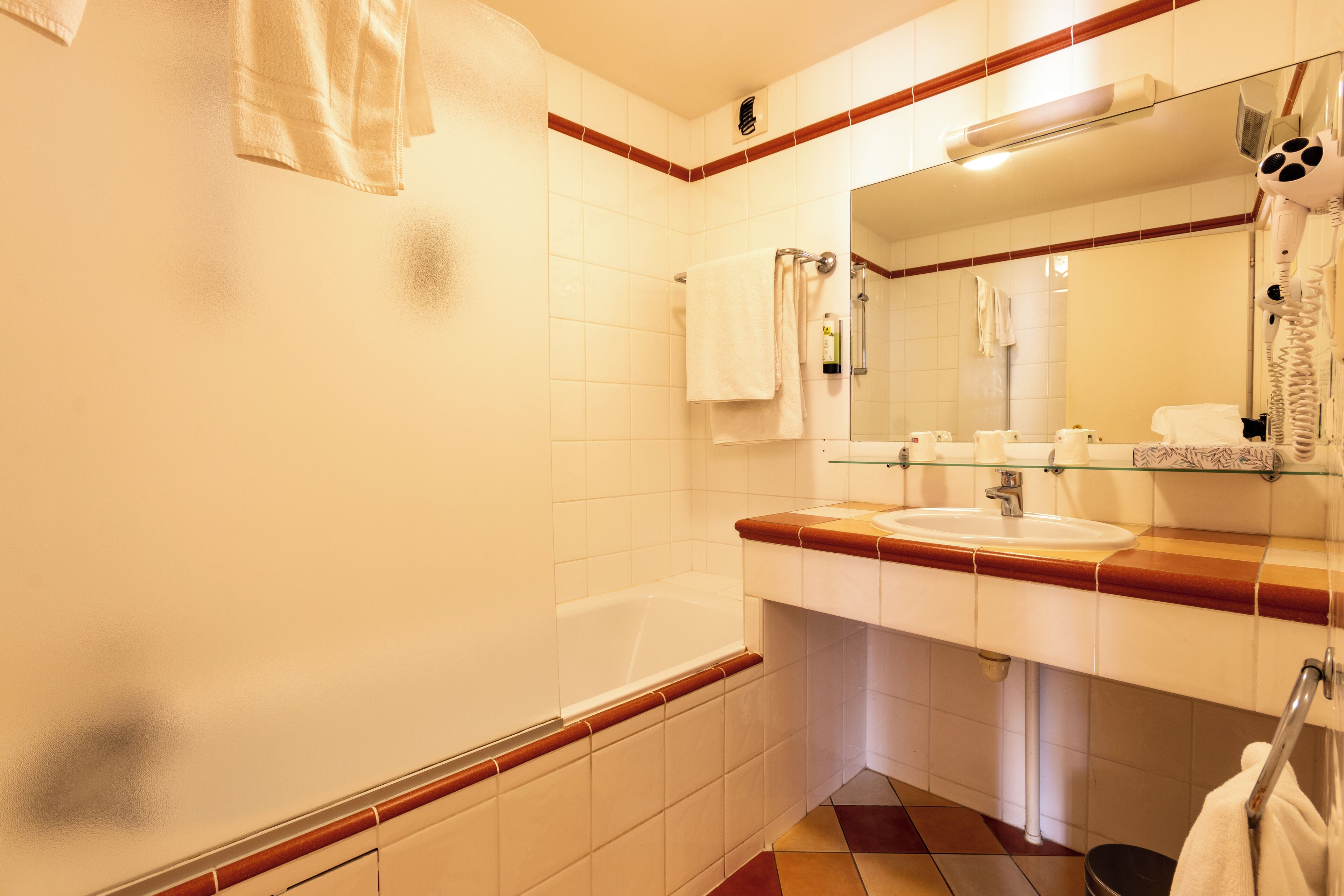 Un baño con bañera, lavamanos, espejo y toallero.