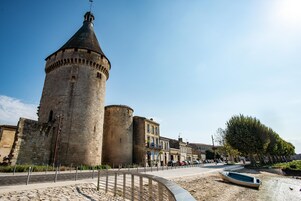 Una torre de piedra histórica con techo cónico, un paseo empedrado y un pequeño bote en la orilla.