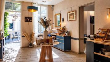 A modern cafe with a wooden table, a vase with dried plants, a coffee machine, and a counter with bread and pastries.