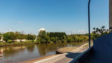 A riverside walkway with a paved path, a railing, and a view of a river and greenery.