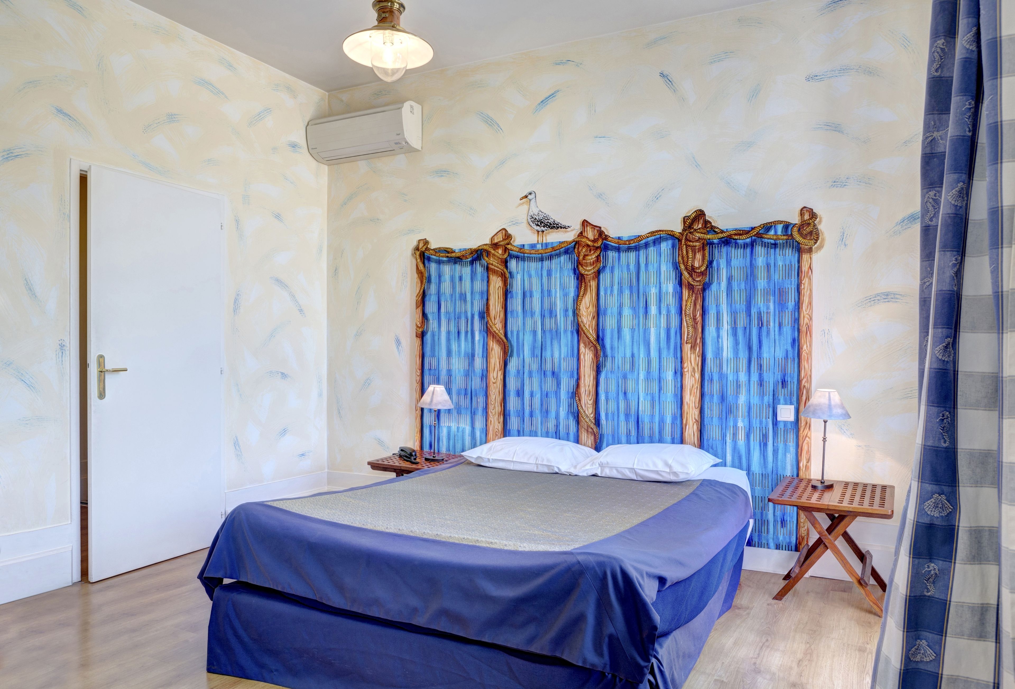 A bedroom with a bed, a nightstand, a lamp, and a curtain with a seagull design.