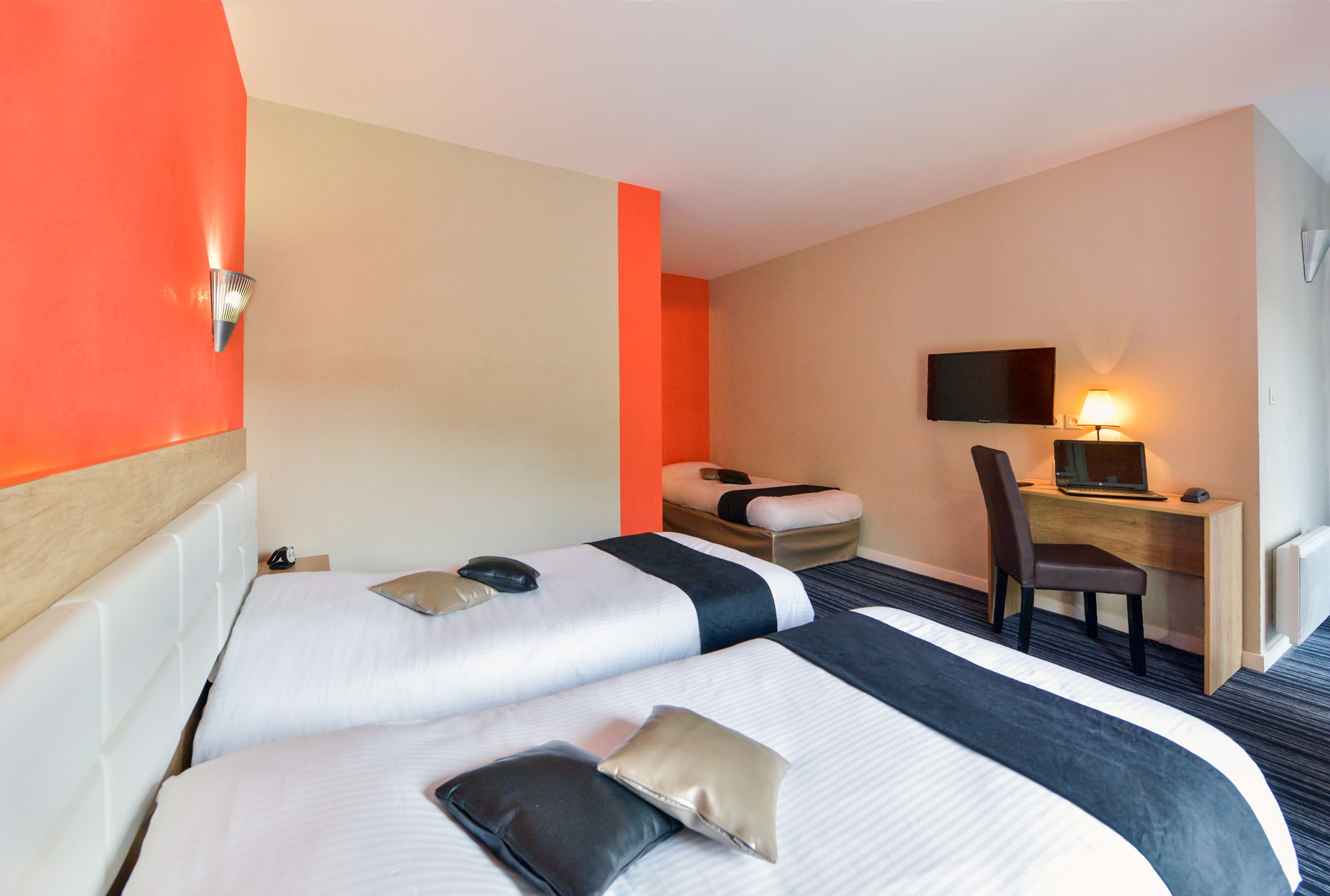 A hotel room with two beds, a desk with a computer, a chair, and a TV on the wall.