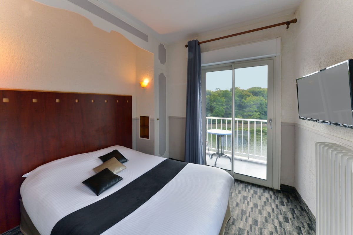 Een hotelkamer met een groot bed, een televisie, een balkon met een tafel en uitzicht op groen.