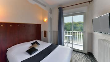 Ein Hotelzimmer mit einem großen Bett, einem Fernseher, einem Balkon mit Tisch und Blick ins Grüne.